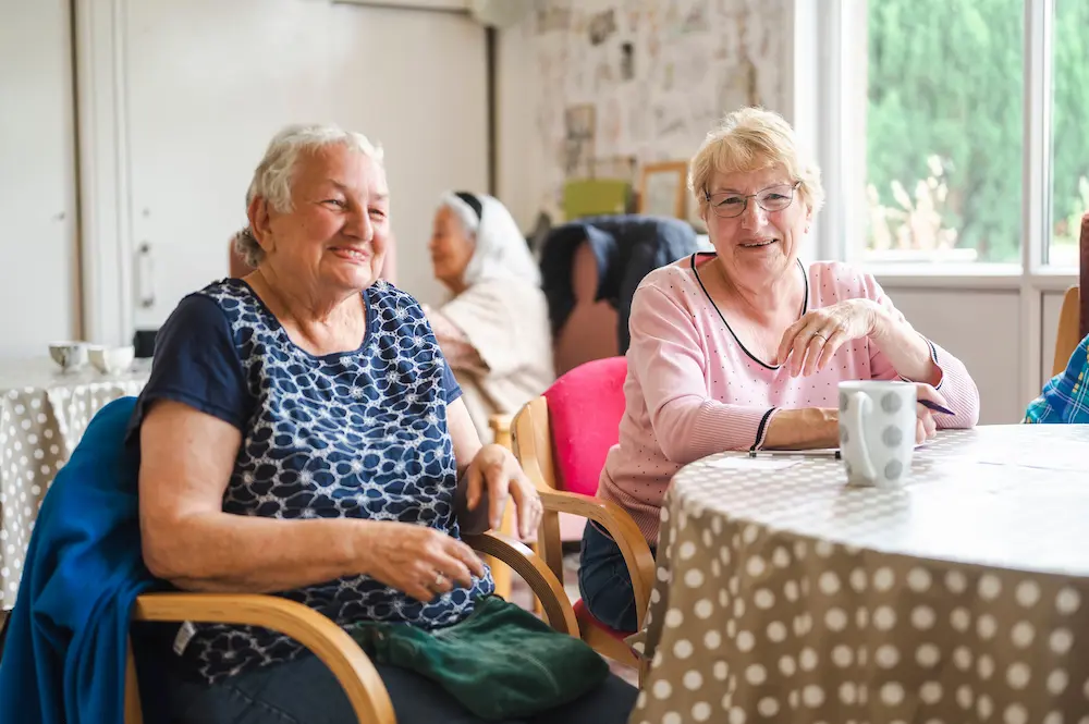 An elderly pair of ladies smiling and drinking tea together