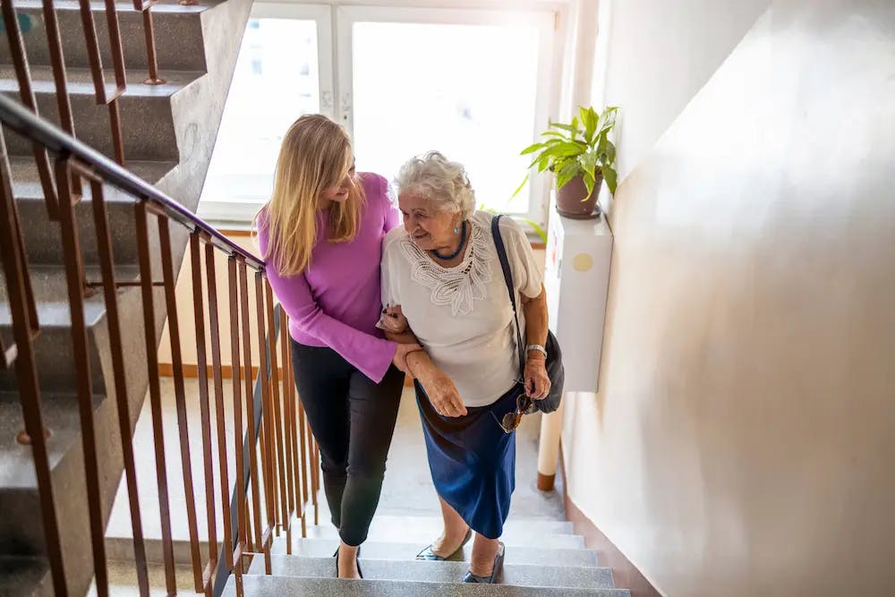 Carer helping older woman up the stairs