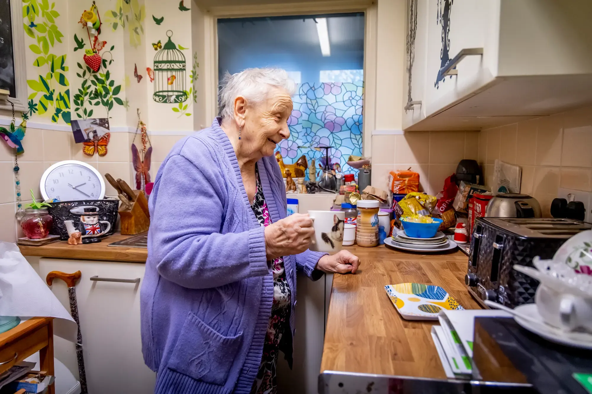 Older woman standing in a kitchen drinking from a mug