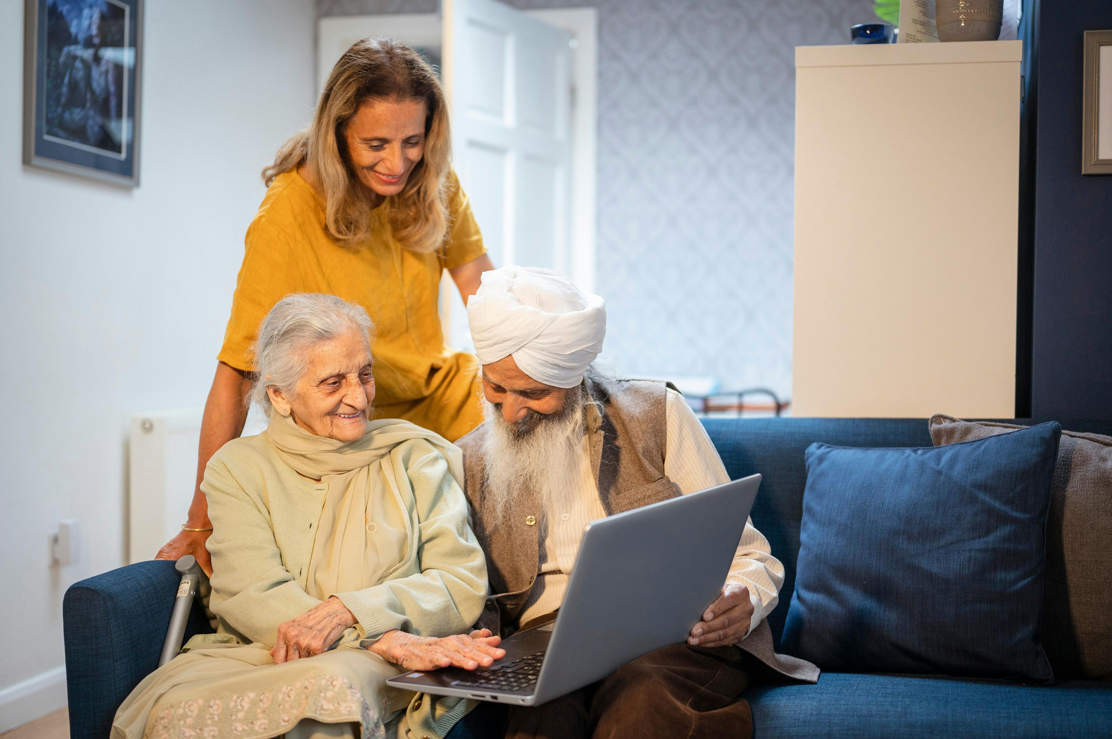 Two older adults using a laptop, being helped by a younger woman