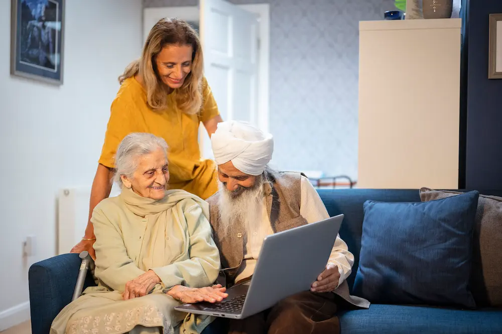 Two older adults using a laptop, being helped by a younger woman